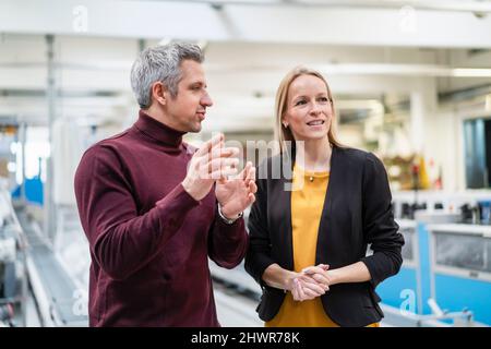 Businessman sharing ideas with blond businesswoman in industry Stock Photo