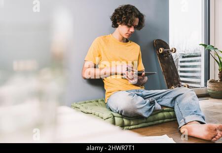 Young man using tablet PC by skateboard at home Stock Photo