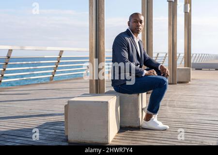 Bald businessman wearing smart casual sitting on bench at promenade Stock Photo