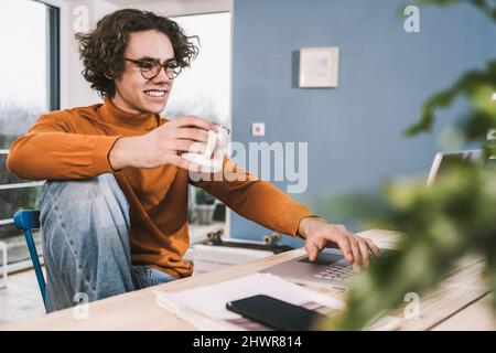 Happy young man holding coffee cup using laptop at home Stock Photo