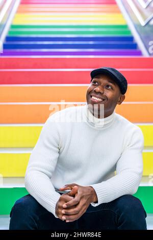 Happy man wearing flat cap sitting on colorful staircase in subway station Stock Photo