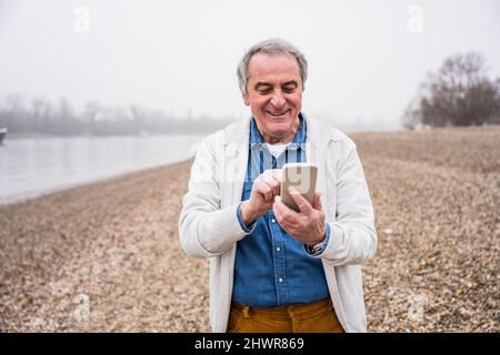 Happy senior man using mobile phone at beach Stock Photo