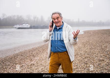Senior man talking on mobile phone gesturing at beach Stock Photo