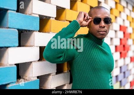 Bald man wearing sunglasses by multi colored brick wall Stock Photo