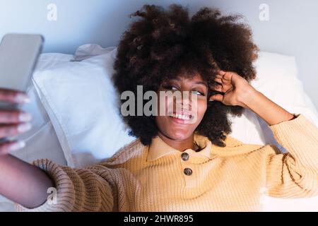 Young woman taking selfie through mobile phone in bedroom Stock Photo
