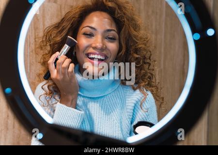 Happy influencer vlogging and applying blusher in front of ring light Stock Photo