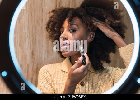 Young influencer applying blusher on cheek in front of ring light Stock Photo