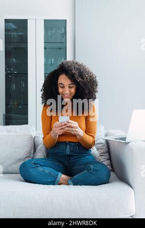 Smiling woman text messaging through mobile phone at home Stock Photo
