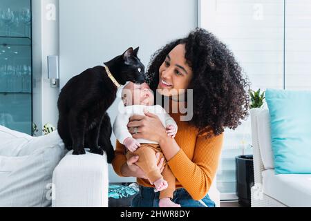 Smiling mother with baby boy looking at cat in living room Stock Photo