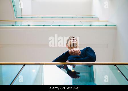 Young man leaning on railing at corridor Stock Photo