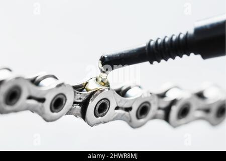 Greasing a bicycle chain with a drop of golden oil close-up on a gray background. Taking care of the bike drive system. Stock Photo