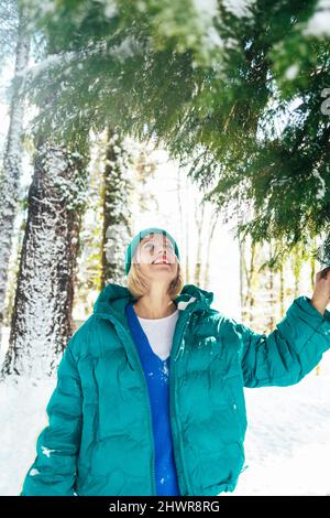 Smiling woman standing below fir tree in winter forest Stock Photo