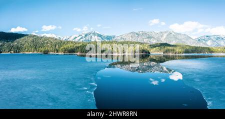 Germany, Bavaria, Aerial view of ice floes thawing in Eibsee lake with Ammergau Alps in background Stock Photo