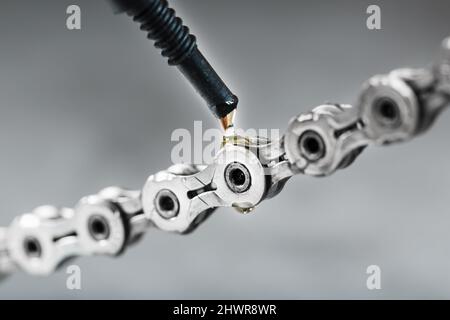 Greasing a bicycle chain with a drop of golden oil close-up on a gray background. Taking care of the bike drive system. Stock Photo