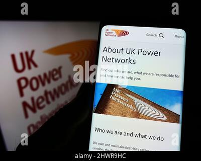 Person holding cellphone with webpage of British electricity company UK Power Networks on screen with logo. Focus on center of phone display. Stock Photo