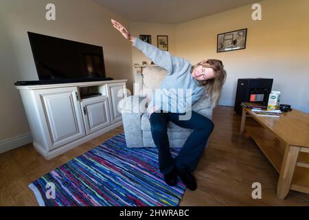 Tall blond woman doing morning stretching exercises in armchair Stock Photo