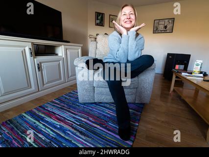 Tall blond woman doing morning stretching exercises in armchair Stock Photo