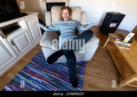 Tall blond woman doing morning stretching exercises in armchair Stock Photo