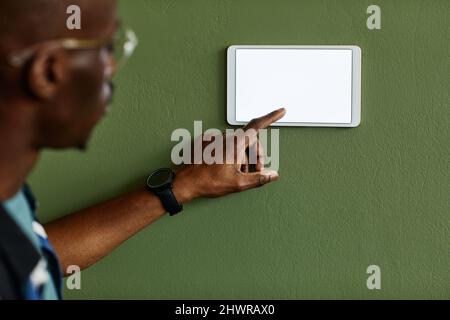 Minimal close up of African American man using smart home control panel with blank screen on green wall, copy space Stock Photo