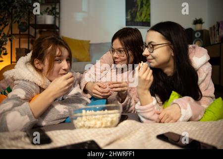 Happy female friends having good time at pajama party in the bedroom. friendship, people, pajama party, entertainment and junk food concept. Stock Photo