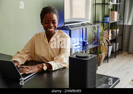 Portrait of smiling African American woman using voice controlled smart speaker while working from home Stock Photo