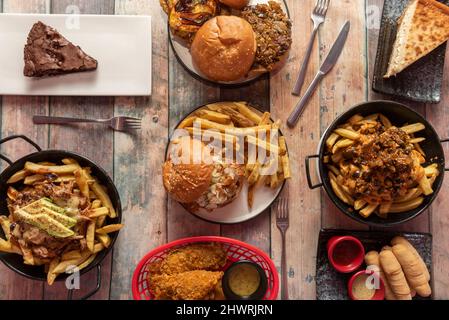 Set of fast food dishes with burgers, fries, tequeños, fried chicken strips, avocado, brownie and cheesecake Stock Photo
