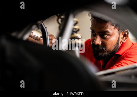 handheld close up head shot shot of bike mechanic reparing motorbike at garage - concept of Hard working, repair service and dedication Stock Photo