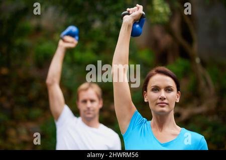 Exercise in fresh air. Shot of a man and woman using kettle bell weights in an outdoor exercise class.