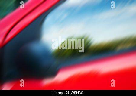 Blurry abstract photo of rural landscape reflected in side window of a red car. Stock Photo