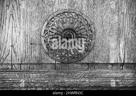 Weathered wooden door with decorative round handle. Aged photo. Black and white. Stock Photo