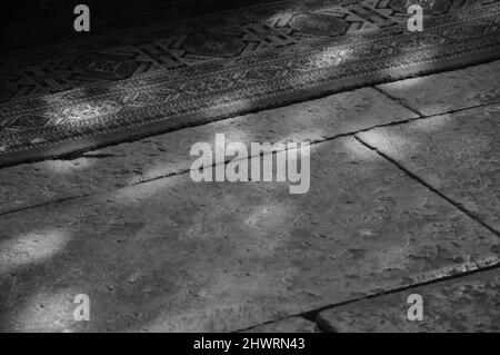 Light spots on the the floor and carpet in church. Sunlight filtered through the stained glass window. A game of light and shadow. Aged photo. Black a Stock Photo