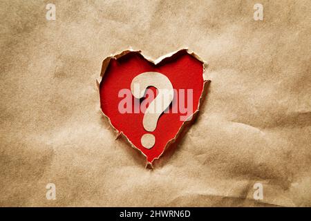 Heart shaped hole in kraft paper. Inside a question mark on a red background. Problem and solution concept. Brainstorm. Stock Photo