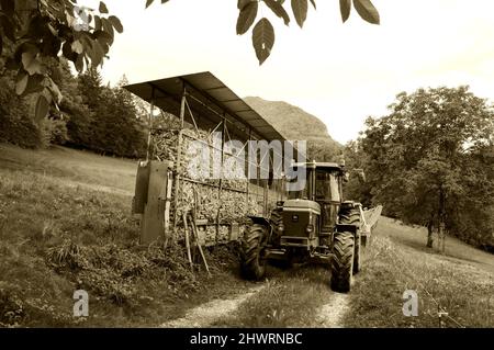 Haute-Savoie, France - August 23, 2015: John Deere 3350 tractor next to corn dryer for animal feeding at small farm. Sepia historic photo Stock Photo