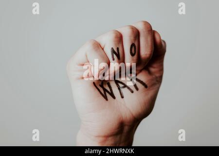 closeup of the clenched fist of a man with the text no war written in it, on an off-white background Stock Photo