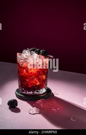 Summer cold cocktail drink with ice garnished with blackberry on dramatic violet background Stock Photo