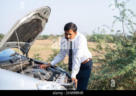 worried businessman checking broken car by lifting car hood on roadside - concept of sadness, worried, accident and problems during road trip Stock Photo