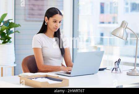 Focused and ready to tackle this day. Shot of a young businesswoman using her laptop at work. Stock Photo
