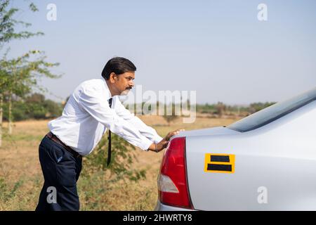 Businessman pusing broken car during hot sunny day - concept of petrol crisis, misfortune and frustration Stock Photo