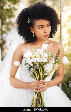 The big day has finally arrived. Shot of a happy and beautiful young bride holding a bouquet of flowers while posing outdoors on her wedding day. Stock Photo
