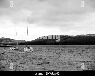 Two Sailing boats moored on Windermere Lake in the Lake District, UK, on a cold and rainy day in black and White Stock Photo