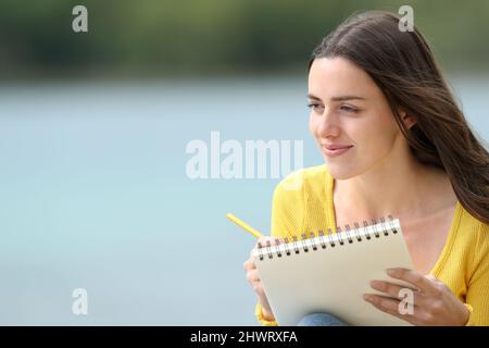 Satisfied woman drawing on notebook sitting in a lake