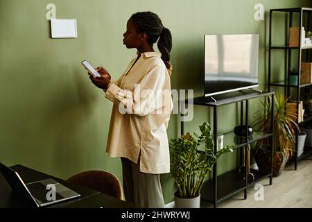 Portrait of young African American woman using smartphone while connecting to smart home system in modern interior Stock Photo