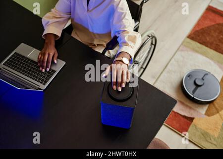 Top view of young black woman in wheelchair using smart speaker while working from home, copy space Stock Photo