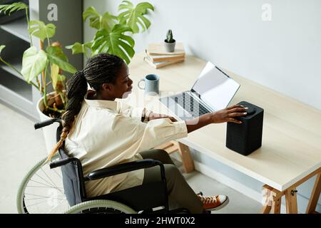 Portrait of African American woman in wheelchair using laptop while working at home office with accessible smart devices Stock Photo