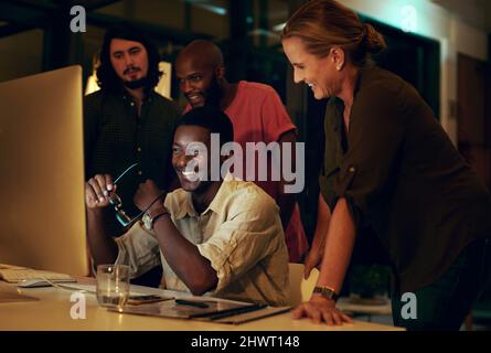 Great things happen when a team works together. Shot of a group of businesspeople looking at something on a computer in an office at night. Stock Photo
