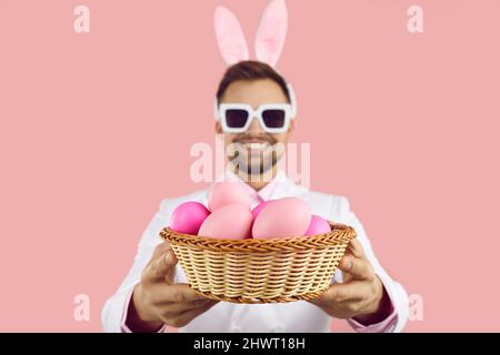 Close up of wicker bowl with painted easter eggs in hands of happy man on pink background. Stock Photo