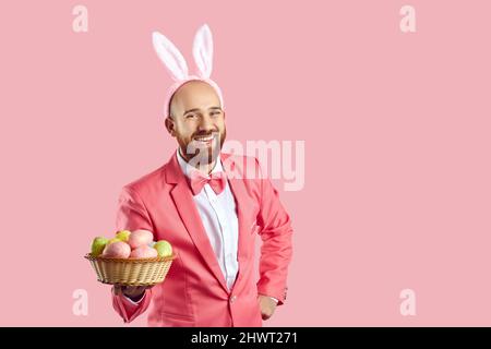 Happy young man in suit and funny bunny ears holding bowl of Easter eggs and laughing Stock Photo