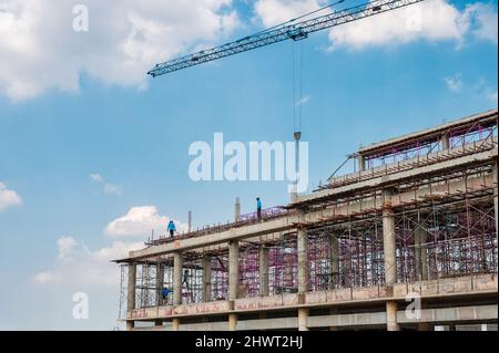 Structure of large building with worker working, crane and scaffold in construction site on sunny day Stock Photo