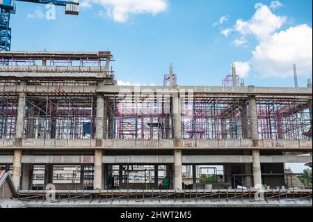 Structure of large building with worker working, crane and scaffold in construction site on sunny day Stock Photo