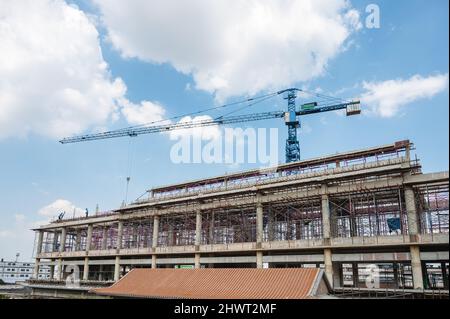 Structure of large building with worker working, crane and scaffold in construction site on sunny day Stock Photo